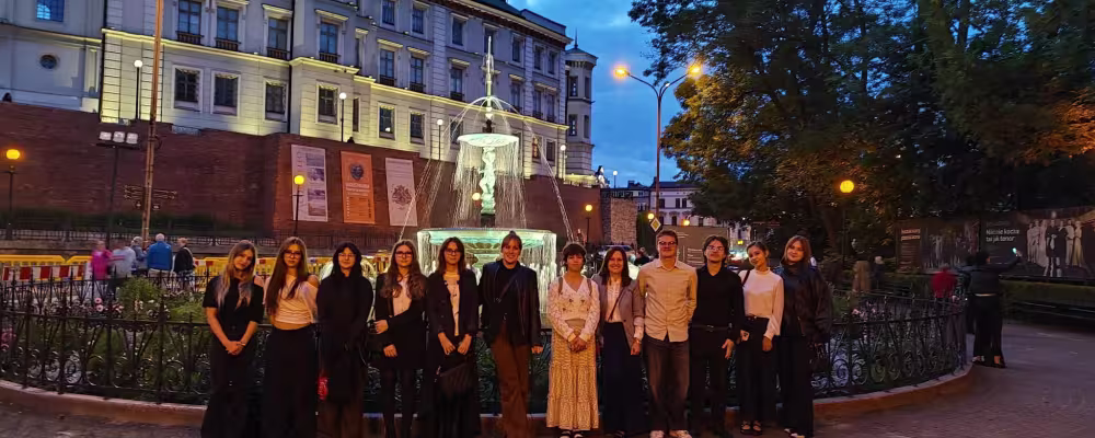Młodzi ludzie przed oświetloną fontanną i budynkiem miejskim o zmierzchu.
